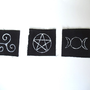 Peut inclure: Trois patchs en tissu noir avec des symboles brodés blancs. Les symboles sont une triple spirale, un pentagramme et une triple lune.