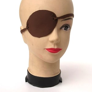 Op de afbeelding: Een bruin leren ooglapje met een verstelbare band. Het ooglapje wordt gedragen over het rechteroog van een mannequinhoofd.