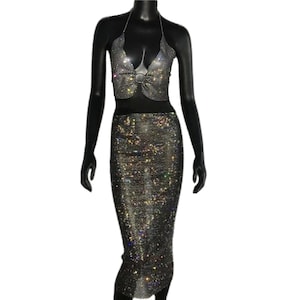 May include: A two-piece outfit featuring a halter top and a skirt, both made of a sparkly, mesh fabric with rhinestones. The top has a bow detail at the center.