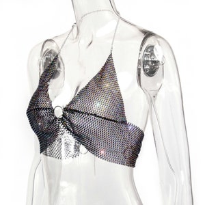 May include: A silver halter top made of a mesh fabric with rhinestones. The top has a ring detail at the center.