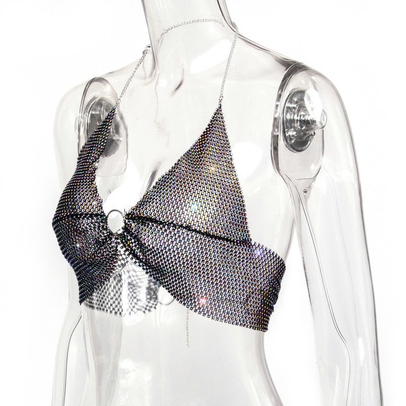 May include: A silver halter top made of a mesh fabric with rhinestones. The top has a ring detail at the center.