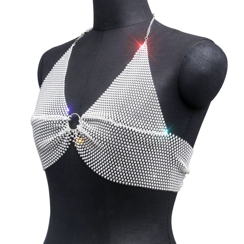 May include: A silver halter top made of a chainmail design with rhinestones. The top has a ring closure at the center.