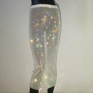 May include: A white skirt made of a mesh fabric with iridescent rhinestones. The skirt is fitted and has a midi length.