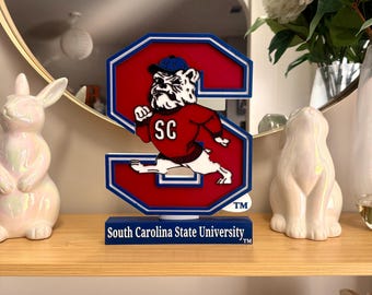 May include: A red, white, and blue decorative sign in the shape of the number 2, featuring the South Carolina State University bulldog mascot. The sign has the text "South Carolina State University" on the base.
