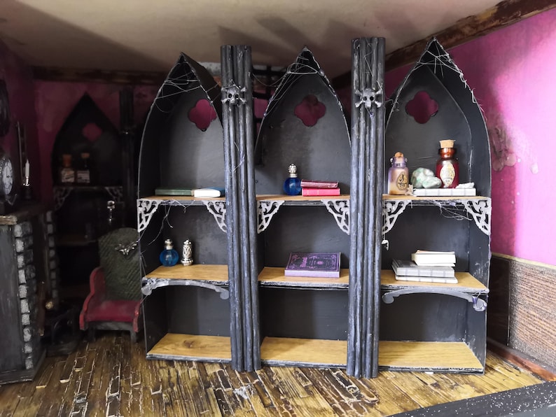 May include: A set of three black gothic-style shelves with arched tops and decorative details. The shelves are filled with various items, including books, bottles, and other decorative objects.