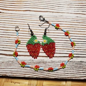 May include: A set of beaded strawberry earrings and a beaded strawberry bracelet. The earrings and bracelet are made with red, green, white, and blue beads.