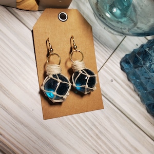 May include: A pair of blue glass ball earrings with white string netting. The earrings have gold hooks.