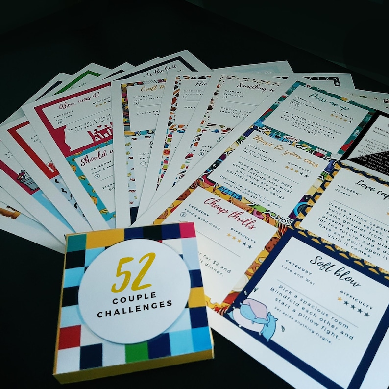 Op de afbeelding: Een set van 52 kleurrijke kaarten met verschillende uitdagingen voor koppels. De kaarten liggen in een waaier, met de doos op de voorgrond. De doos is wit met een rood, geel, blauw en groen geruit patroon en de tekst "52 COUPLE CHALLENGES".