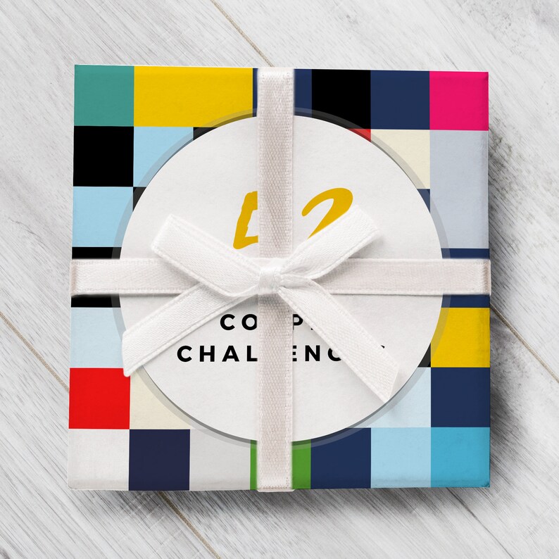 Op de afbeelding: Een witte cadeaudoos met een kleurrijk geometrisch patroon en een wit lint dat in een strik is gebonden. De doos heeft een witte ronde sticker met het nummer "42" in gele tekst en de woorden "CO-OP CHALLENGE" in zwarte tekst.