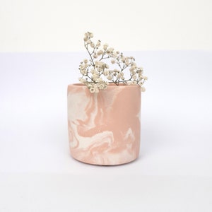 May include: A pink and white marbled ceramic vase with a small bouquet of white flowers.