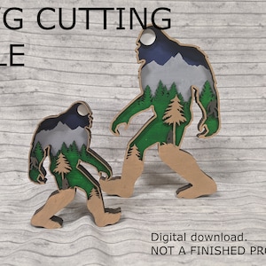 May include: Two layered wood cutouts of Bigfoot walking with a forest scene inside. The larger Bigfoot is brown with a blue and green forest scene. The smaller Bigfoot is brown with a gray and green forest scene. The text "SVG CUTTING FILE" is at the top of the image.