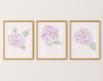 May include: Three framed floral art prints. Each print features a watercolor hydrangea in shades of pink and green against a pink and white striped background. The frames are gold.