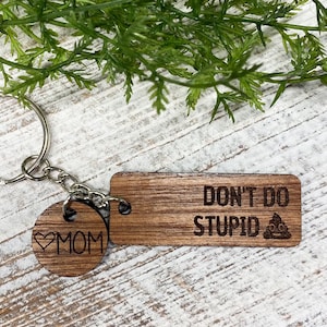 May include: Wooden keychain with a heart and the word "MOM" on one side and a rectangular tag with the text "DON'T DO STUPID" and a poop emoji on the other side.