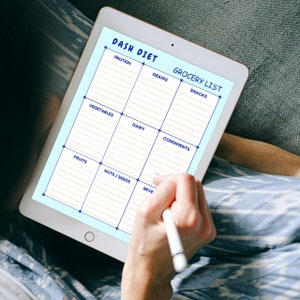 May include: A digital tablet displaying a grocery list template for the DASH diet. The template is divided into categories such as protein, grains, vegetables, dairy, condiments, fruits, nuts/seeds, and beverages.