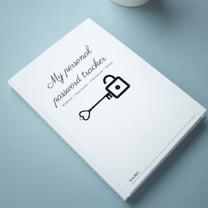 May include: A white personal password tracker notebook with black text and a key and lock graphic. The cover reads "My personal password tracker" with fields for website, username, password, and notes. The notebook is on a light blue surface.