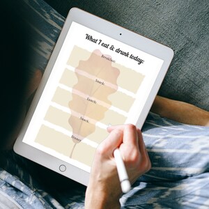 May include: A digital tablet with a white background and a brown leaf design. The text "What I eat & drunk today" is at the top of the screen. The text "Breakfast", "Snack", "Lunch", "Snack", and "Dinner" are listed below the leaf design.