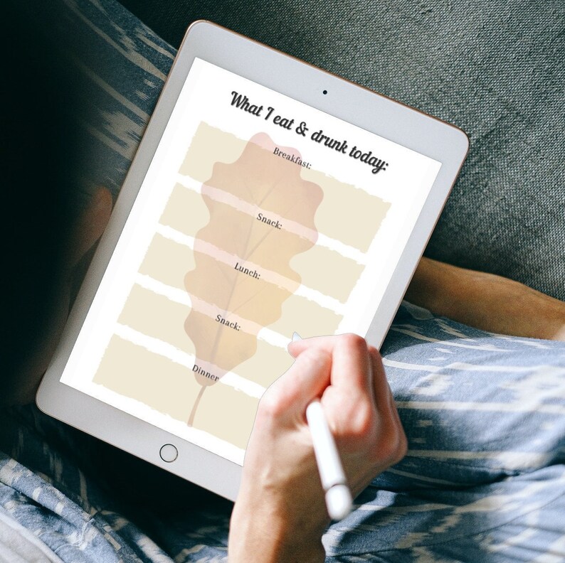 May include: A digital tablet with a white background and a brown leaf design. The text "What I eat & drunk today" is at the top of the screen. The text "Breakfast", "Snack", "Lunch", "Snack", and "Dinner" are listed below the leaf design.
