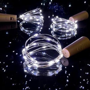 Könnte beinhalten: Lichterkette mit weißen LED-Lampen auf einem dünnen Silberdraht, aufgerollt um einen braunen Korken. Die Lichter werden mit Batterien betrieben und befinden sich auf einer reflektierenden schwarzen Oberfläche.