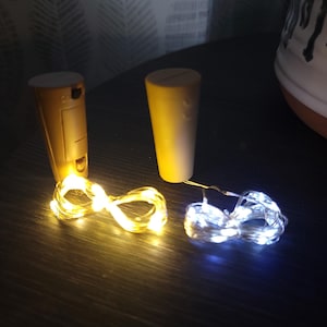 Può includere: Due tappi per bottiglie a forma di sughero con luci a stringa attaccate. Un tappo ha un vano batteria. Le luci a stringa sono di colore giallo caldo e bianco freddo. Le luci sono disposte a forma di otto.
