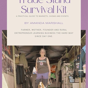 May include: A book cover titled Trade Stand Survival Kit: A Practical Guide to Markets, Shows and Events by Amanda Marshall. The cover features a photograph of a person standing in a trade stall with a basset hound, surrounded by clothing and displays.