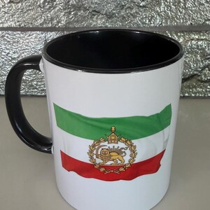 May include: White ceramic mug with a black handle and interior. The mug features the Iranian flag design, with green, white, and red stripes, and a golden emblem. The mug is a standard size for hot beverages.