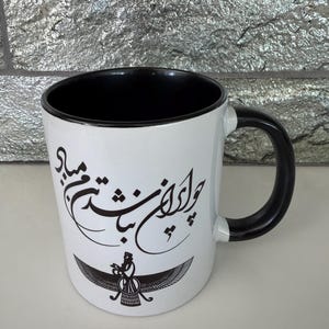 May include: White ceramic mug with a black interior and handle. The mug features black calligraphy and a stylized bird emblem. The mug is designed for hot beverages and is suitable for home or office use.