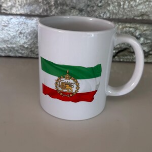 May include: White ceramic mug featuring the Iranian flag design. The flag design includes green, white, and red stripes, with a golden emblem in the center. The mug has a curved handle and is suitable for hot beverages.