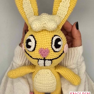 May include: A handmade yellow crochet bunny with large ears, black and white eyes, and a pink heart-shaped nose. The bunny has a white chef's hat and pink accents on its feet. The word "ENGLISH" is visible in the image.