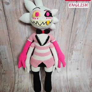 May include: A crocheted plush toy of a character with white hair, pink and white striped clothing, and a pink bow tie. The character has a large, toothy grin and pink and yellow eyes.