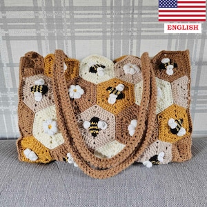 Könnte beinhalten: Eine gehäkelte Tragetasche mit einem Wabenmuster in Braun, Gelb und Weiß. Die Tasche ist mit gehäkelten Bienen und Gänseblümchen verziert.