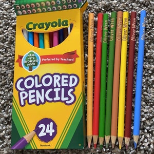 May include: A box of Crayola coloured pencils with the text "COLORED PENCILS" and "24" on the front. Several personalised pencils with the name "Oliver Wren" are next to the box. The text "personalized color pencils" is at the bottom.