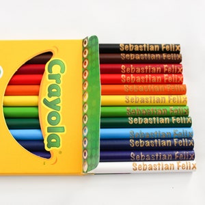 May include: A box of Crayola coloured pencils, with the brand name in green. The pencils are in various colours, including red, orange, yellow, green, and blue. Each pencil is labelled with the name "Sebastian Felix". The box is yellow and has text that says "Made with reforested wood".