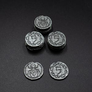Peut inclure: Collection de jetons de jeu argent&eacute;s antiques. Les jetons pr&eacute;sentent un motif d'araign&eacute;e et le chiffre "5" avec des volutes d&eacute;coratives. Les jetons sont empil&eacute;s en petits tas et dispos&eacute;s sur une surface sombre.