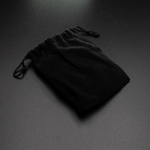 Peut inclure: Un sac en velours noir avec cordon de serrage, id&eacute;al pour les bijoux ou les petits cadeaux. Le sac est ferm&eacute; par un cordon noir et pos&eacute; sur un fond sombre.