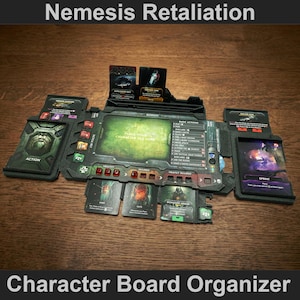 May include: A black character board organiser for the board game Nemesis Retaliation. The organiser has multiple compartments for cards and tokens, with the text "Nemesis Retaliation" and "Character Board Organizer".
