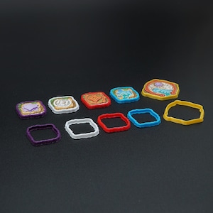 May include: A collection of colorful, small, square-shaped game pieces and matching square frames. The game pieces have various designs and colors, including purple, white, red, blue, and yellow. The frames are purple, white, red, and blue, and yellow.