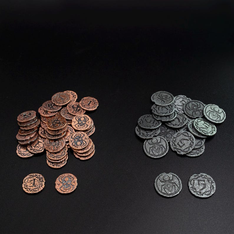 Peut inclure: Deux ensembles de pi&egrave;ces de jeu en m&eacute;tal. L'un est de couleur cuivre, l'autre est gris. Chaque pi&egrave;ce porte un num&eacute;ro et un motif d'araign&eacute;e. Les pi&egrave;ces sont empil&eacute;es et &eacute;parpill&eacute;es sur une surface noire.