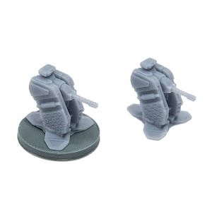 May include: Two gray miniature turrets, likely for a tabletop game, are displayed against a white background. One turret is mounted on a circular base, while the other sits directly on the surface. The turrets have detailed, angular designs.