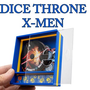 May include: A blue and yellow Dice Throne X-Men game box. The box contains game components, including dice and circular character cards. The box has a clear plastic cover and the text "DICE THRONE X-MEN" is displayed at the top.