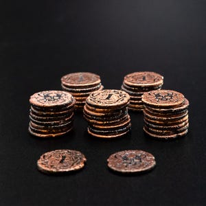 Peut inclure: Plusieurs piles de pi&egrave;ces de monnaie de couleur cuivre avec des gravures d&eacute;taill&eacute;es. Les pi&egrave;ces sont dispos&eacute;es en petits tas et dispers&eacute;es sur une surface sombre. Les pi&egrave;ces ont un aspect vieilli et antique, possiblement pour un jeu ou une collection.