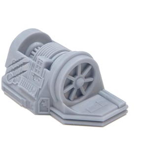 Op de afbeelding: Een grijs plastic model van een kleine industriële machine met een groot tandwiel en een klein bedieningspaneel. De machine heeft een grijze basis en een grijs metalen frame.