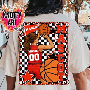 May include: Cream-colored t-shirt featuring a basketball mascot design. The design includes a basketball player in a red uniform, basketballs, stars, and the word "MASCOT". The design is framed with a black and white checkered pattern.