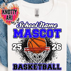 May include: White t-shirt with a basketball-themed design. The design includes the words "School Name", "Mascot", and "Basketball" in blue and white. A basketball is shown going through the net, with the numbers 25 and 26 on either side.
