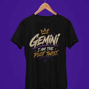 May include: A black short-sleeve t-shirt featuring a graphic print with a gold crown above the word GEMINI in a distressed font, followed by the text I AM THE PLOT TWIST in gold, with the small text SOULFUL XPRESSION and an X symbol below.