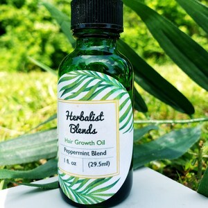 Op de afbeelding: Een groene glazen fles met een zwarte druppelaar. De fles heeft een wit etiket met de tekst "Herbalist Blends" en "Hair Growth Oil Peppermint Blend 1 fl. oz (29.5ml)".