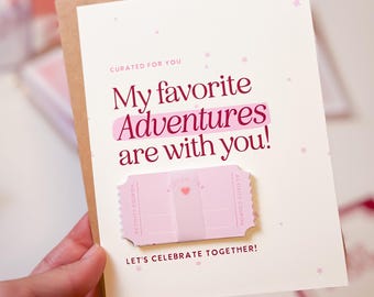 Peut inclure: Une carte de vœux avec un fond beige clair et une enveloppe marron. La carte indique "My favorite Adventures are with you!" en texte rose, avec un graphique de billet rose. Le texte "Let's celebrate together!" est en bas.