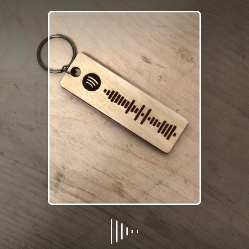 以下が含まれることがあります： Spotifyのロゴと刻まれたバーコードが付いた木製キーホルダー。キーホルダーはシルバーのキーリングに取り付けられています。