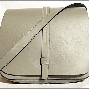 May include: A gray leather satchel bag with a long adjustable strap. The bag has a flap closure and a single buckle.