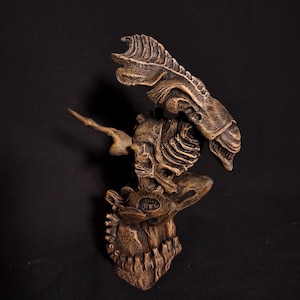 May include: A detailed, brown sculpture of a creature with a skeletal appearance. The sculpture has a textured surface and is set against a black background. The design features intricate details, suggesting a fantasy or science fiction theme.