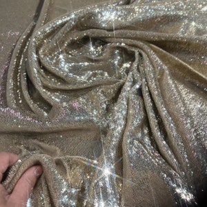 May include: A close-up of a shimmering gold fabric with a subtle iridescent sheen. The fabric is made of sequins and has a soft, drapey texture.